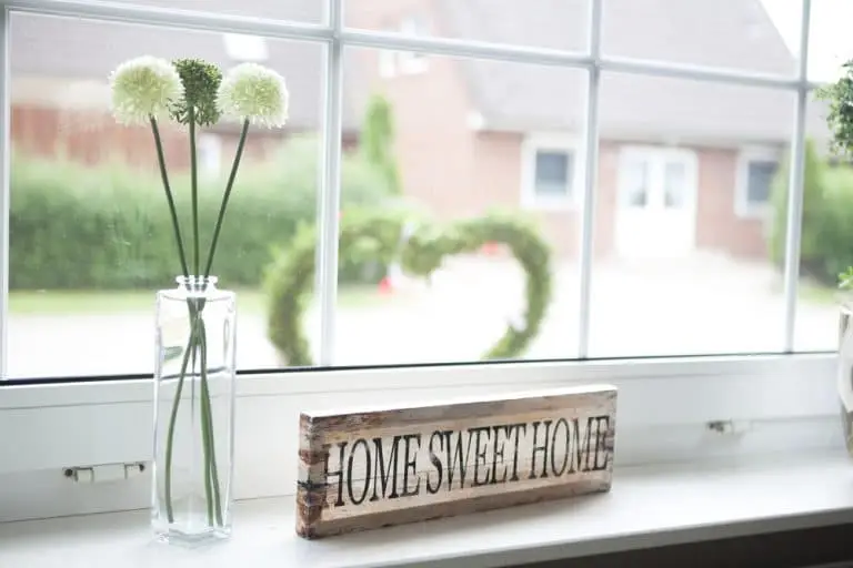 A rustic Home Sweet Home sign beside a vase of flowers on a windowsill